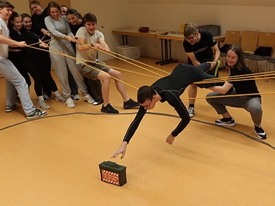 Eine Gruppe baut mit Holzbalken eine Brücke.