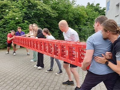 Eine Gruppe transportiert einen horizontalen Kistenstapel.