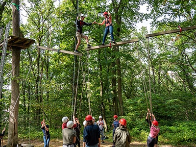 Zwei Auszubildende überwinden mit Hilfe ihrer Gruppe einen Abgrund im Hochseilgarten.
